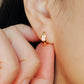 Close-up of a woman's ear wearing gold-plated sterling silver evil eye opal huggie earrings with a dainty minimalist design.