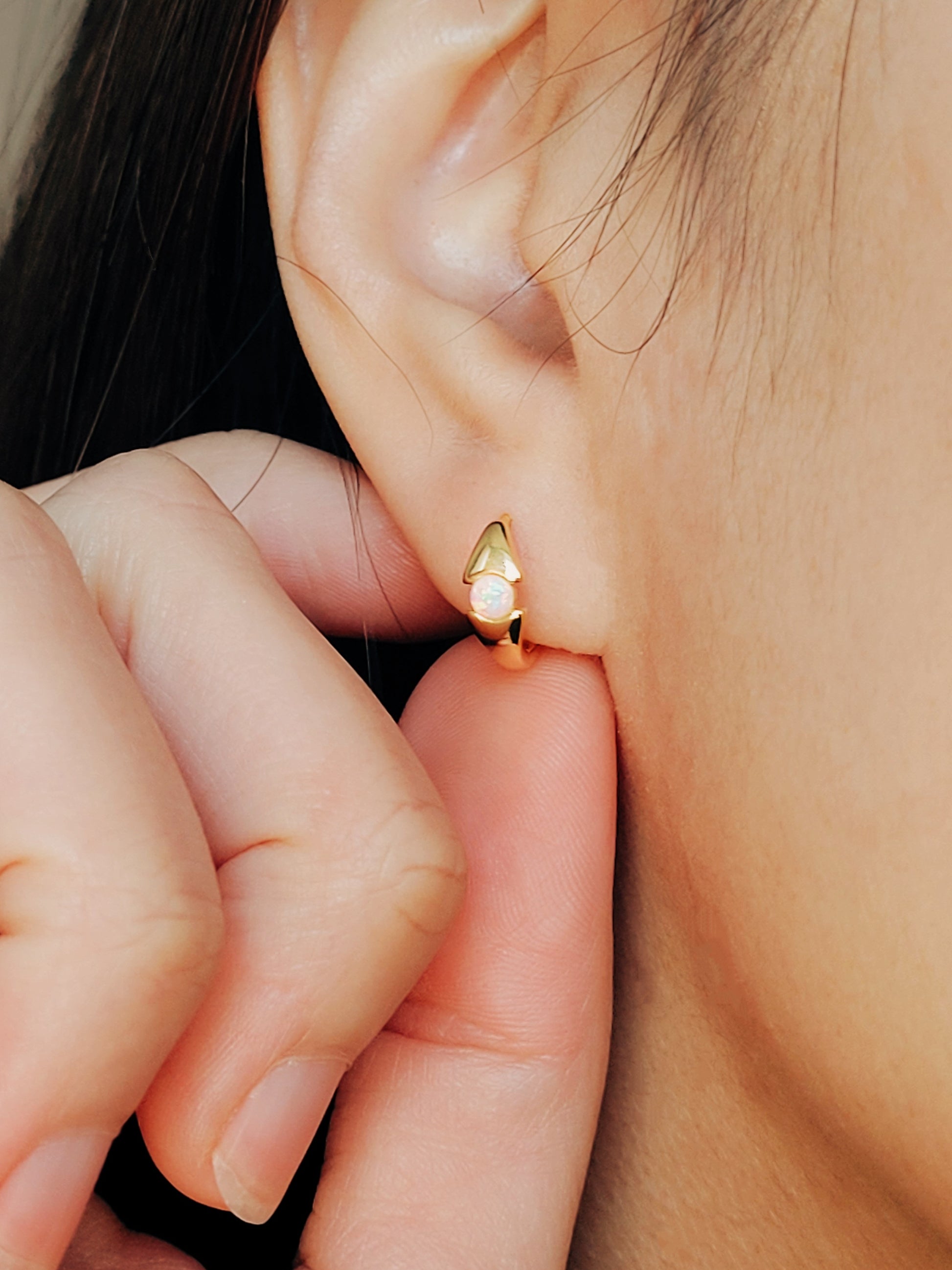 Close-up of a woman's ear wearing gold-plated sterling silver evil eye opal huggie earrings with a dainty minimalist design.