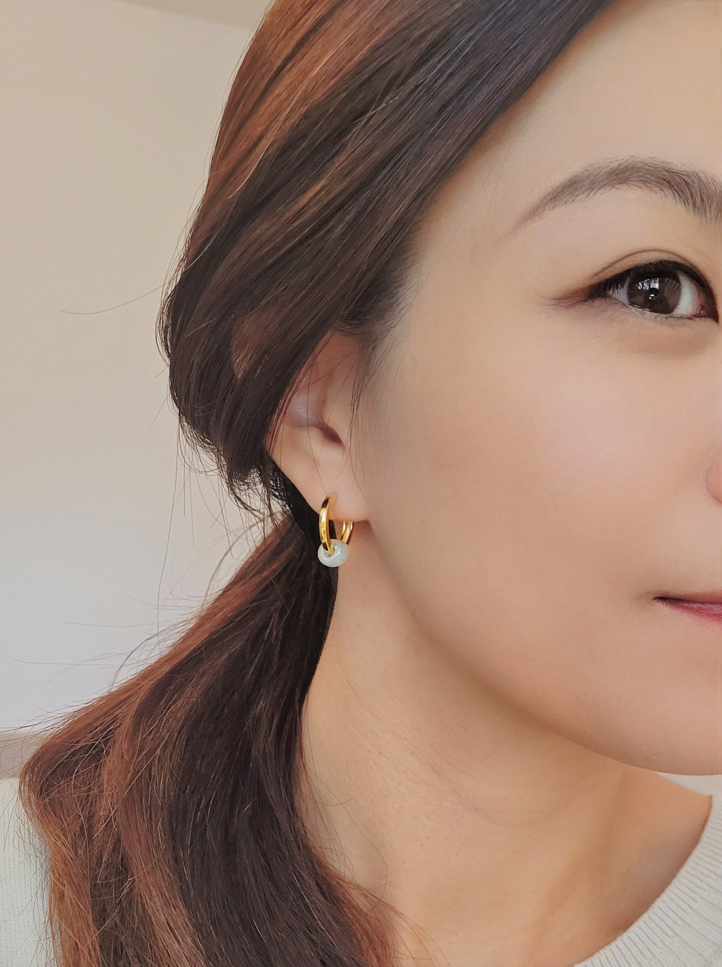 A woman in a cozy white sweater, adorned with stunning 18ct gold jade hoop earrings, radiates elegance and style.