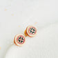 Closeup of retro-style stud earrings featuring a pink and dark green geometric tile pattern with gold accents. These vintage-inspired enamel earrings offer a classic, timeless design adding a touch of elegance to any outfit.