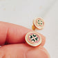 Closeup of retro-style stud earrings featuring a pink and dark green geometric tile pattern with gold accents. These vintage-inspired enamel earrings offer a classic, timeless design adding a touch of elegance to any outfit.