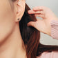 Close-up of a woman’s ear wearing a pair of Retro Gothic tile pattern enamel stud earrings in pink, dark green, and gold. The intricate design features a vintage-style pattern with a bold color combination, creating a striking and elegant look.