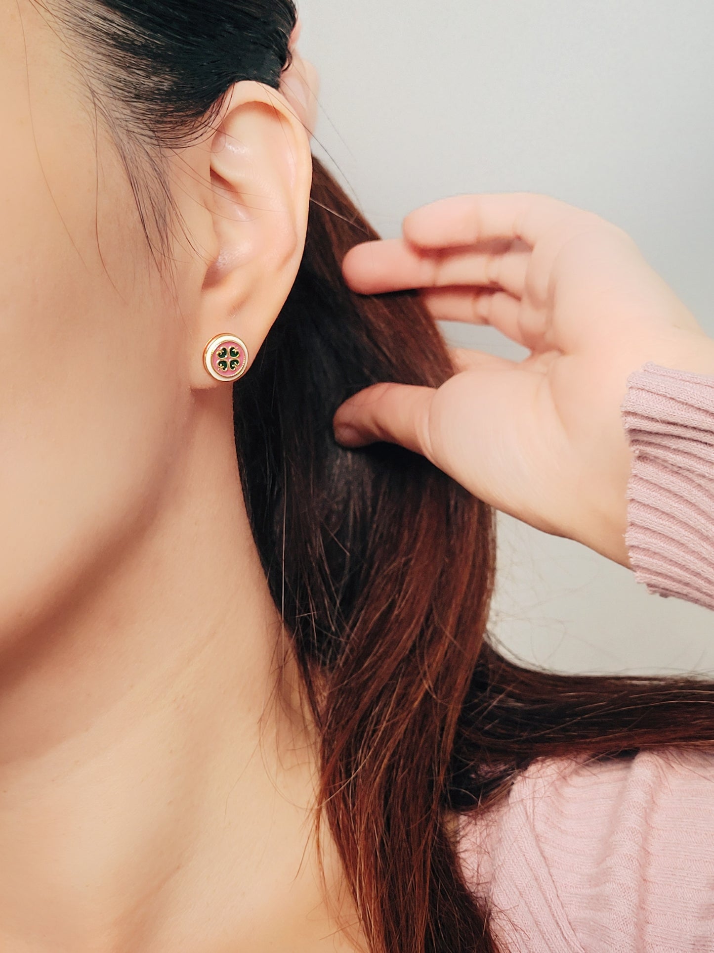 Close-up of a woman’s ear wearing a pair of Retro Gothic tile pattern enamel stud earrings in pink, dark green, and gold. The intricate design features a vintage-style pattern with a bold color combination, creating a striking and elegant look.