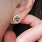 Close-up of a woman’s ear wearing a pair of Retro Gothic tile pattern enamel stud earrings in pink, dark green, and gold. The intricate design features a vintage-style pattern with a bold color combination, creating a striking and elegant look.