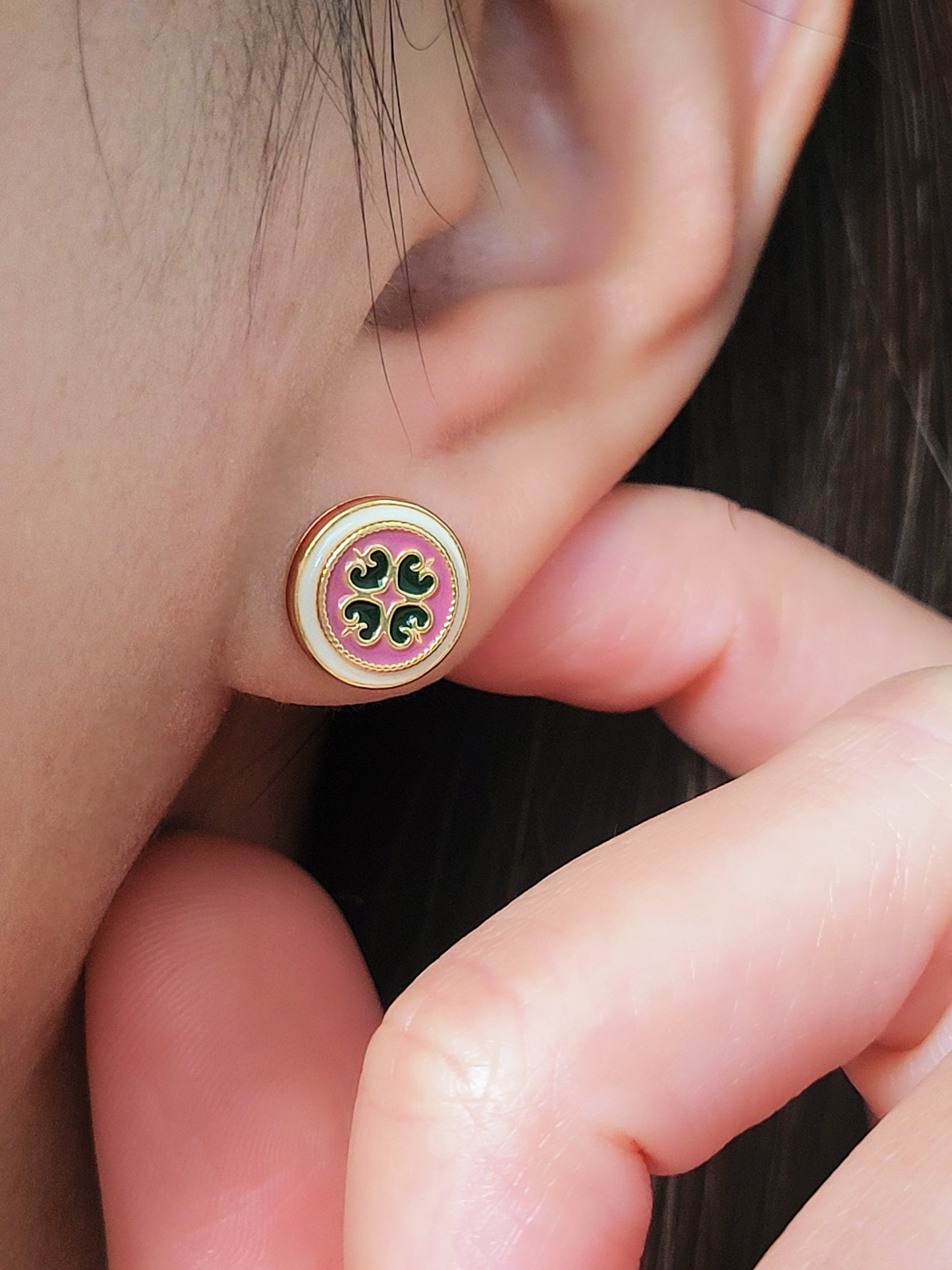 Close-up of a woman’s ear wearing a pair of Retro Gothic tile pattern enamel stud earrings in pink, dark green, and gold. The intricate design features a vintage-style pattern with a bold color combination, creating a striking and elegant look.