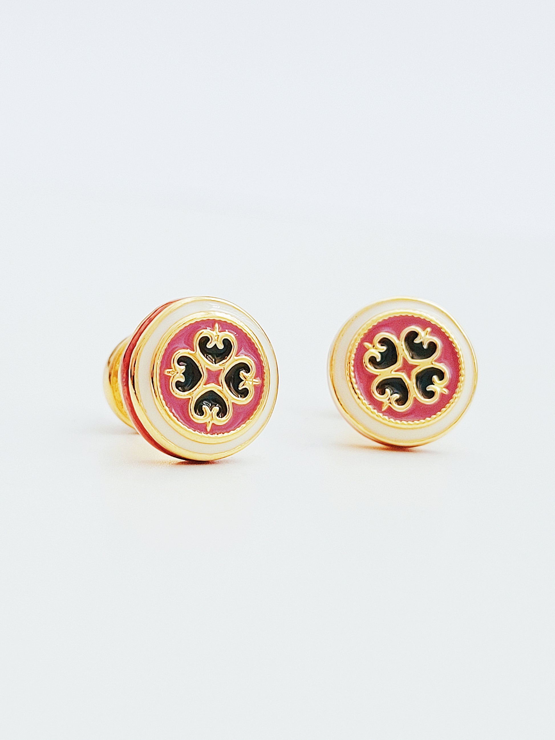 Close up of retro-style stud earrings featuring a pink and dark green geometric tile pattern with gold accents. These vintage-inspired enamel earrings offer a classic, timeless design adding a touch of elegance to any outfit.