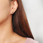 Close-up of a woman’s ear wearing a pair of Retro Gothic tile pattern enamel stud earrings in pink, dark green, and gold. The intricate design features a vintage-style pattern with a bold color combination, creating a striking and elegant look.