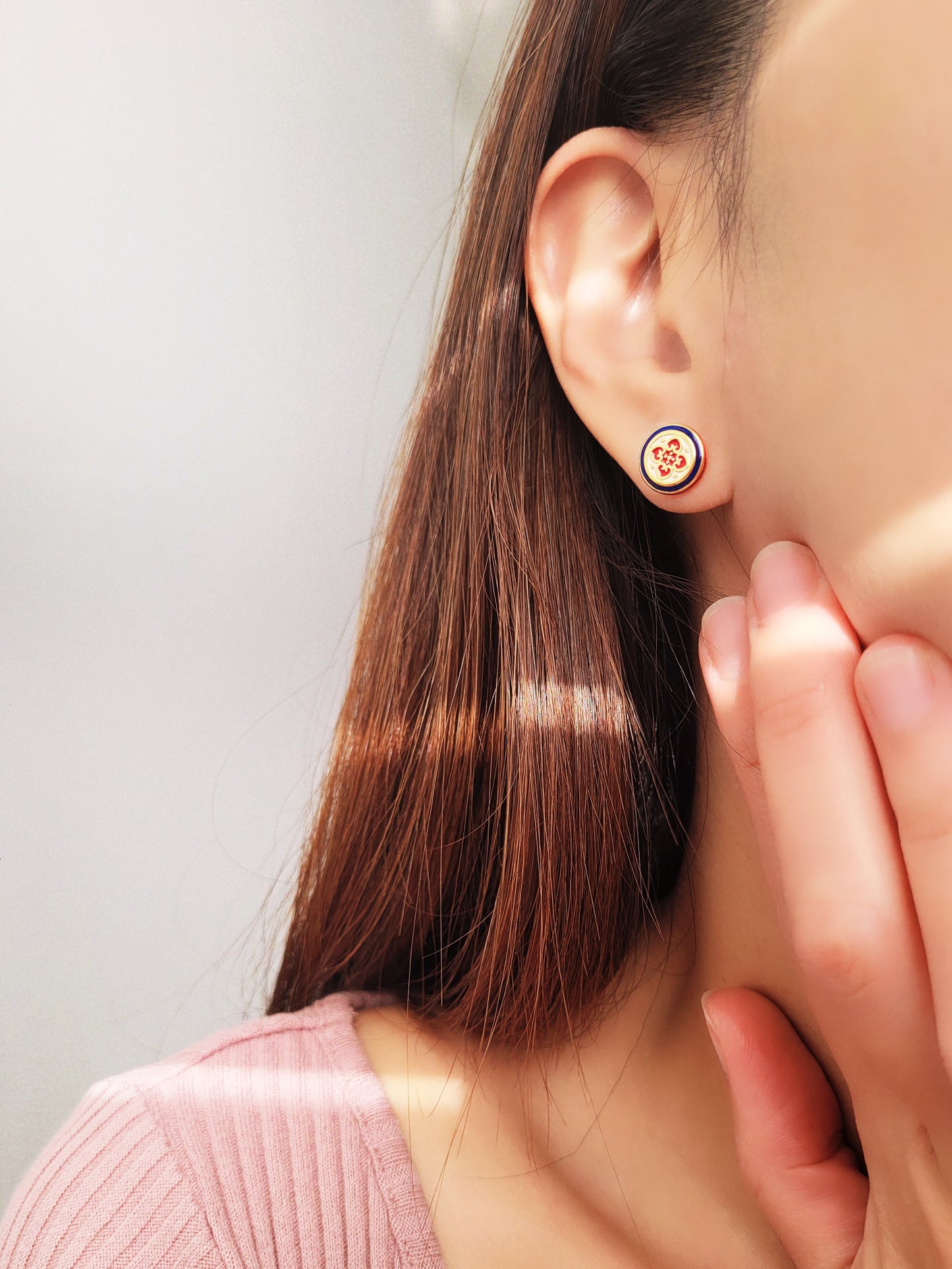 Close-up of a woman's ear wearing a pair of Retro Gothic tile pattern enamel stud earrings in red, blue, and gold. The intricate design features a vintage-style pattern with a bold color combination, creating a striking and elegant look."