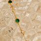 A dainty minimalist green onyx bracelet placed on an aesthetic beige glass surface.
