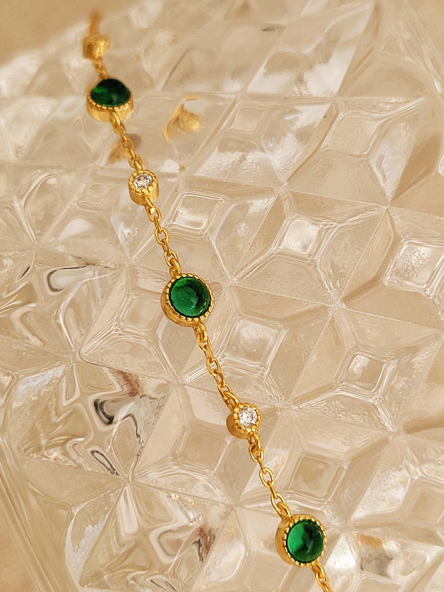 A dainty minimalist green onyx bracelet placed on an aesthetic beige glass surface.