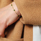 Close-up of a hand wearing a minimalist gold bracelet with green beads, against a brown fabric background.