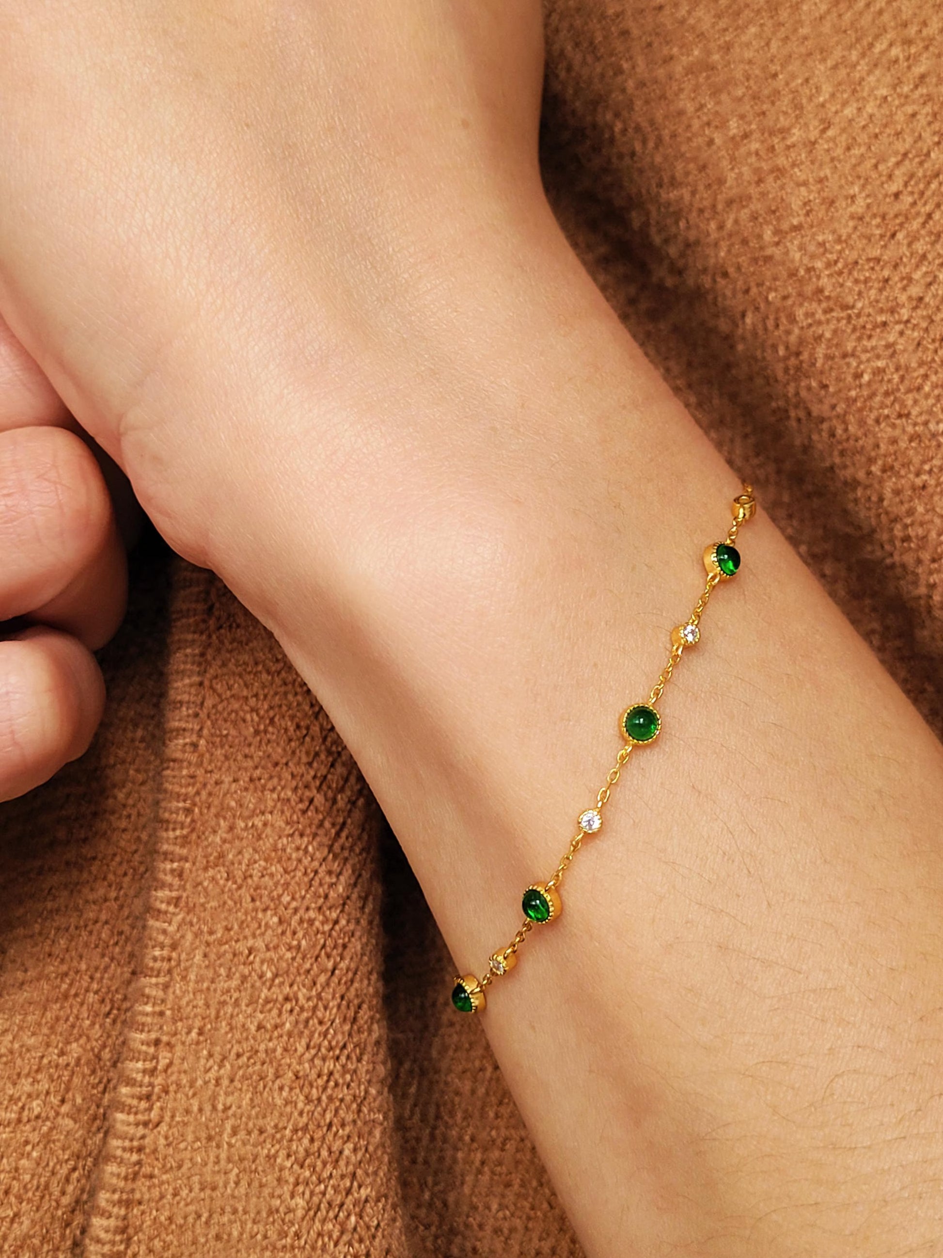 Gold bracelet with green onyx  gemstones on a wrist against a brown fabric background