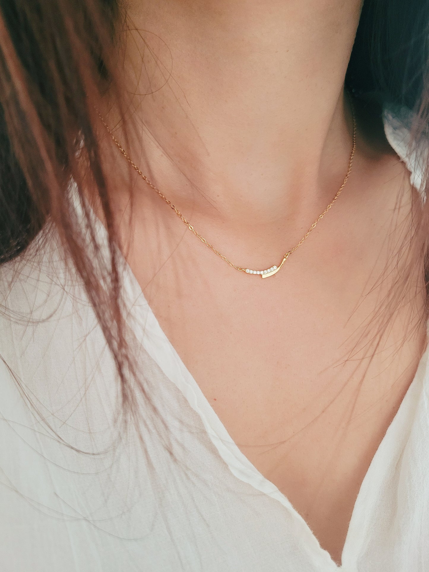 Woman wearing a simple gold bar necklace, dainty and minimalist style.