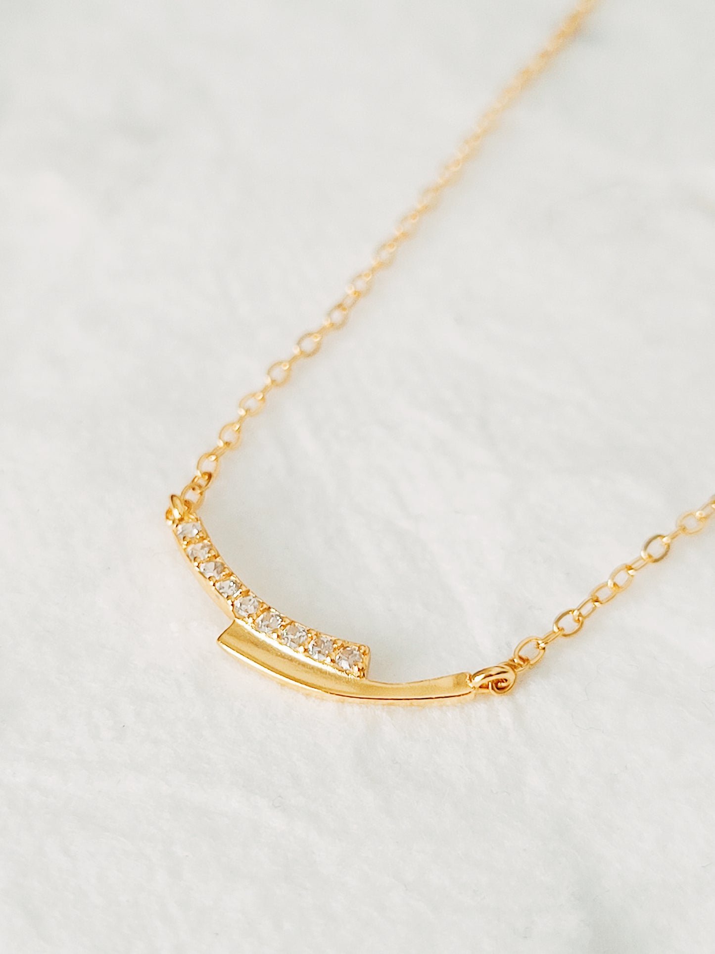 Close up of a simple gold bar necklace with cubic zirconia accents, symbolizes love and unity.