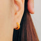 Close-up of an ear wearing an orange enamel gold hoop earring 
