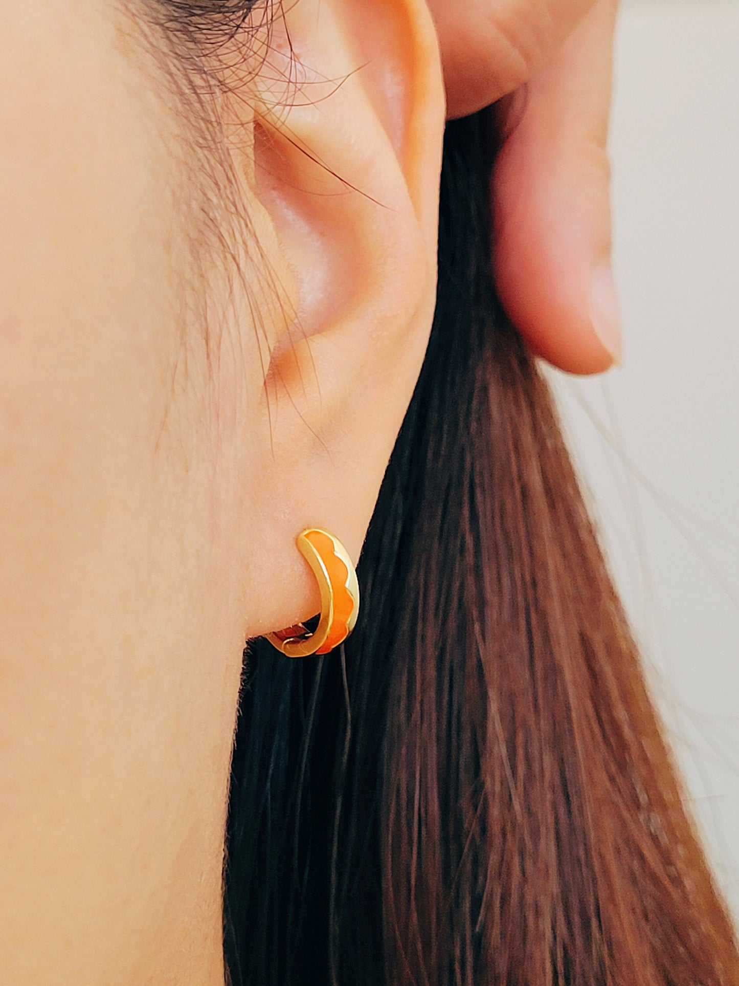 Close-up of an ear wearing an orange enamel gold hoop earring 