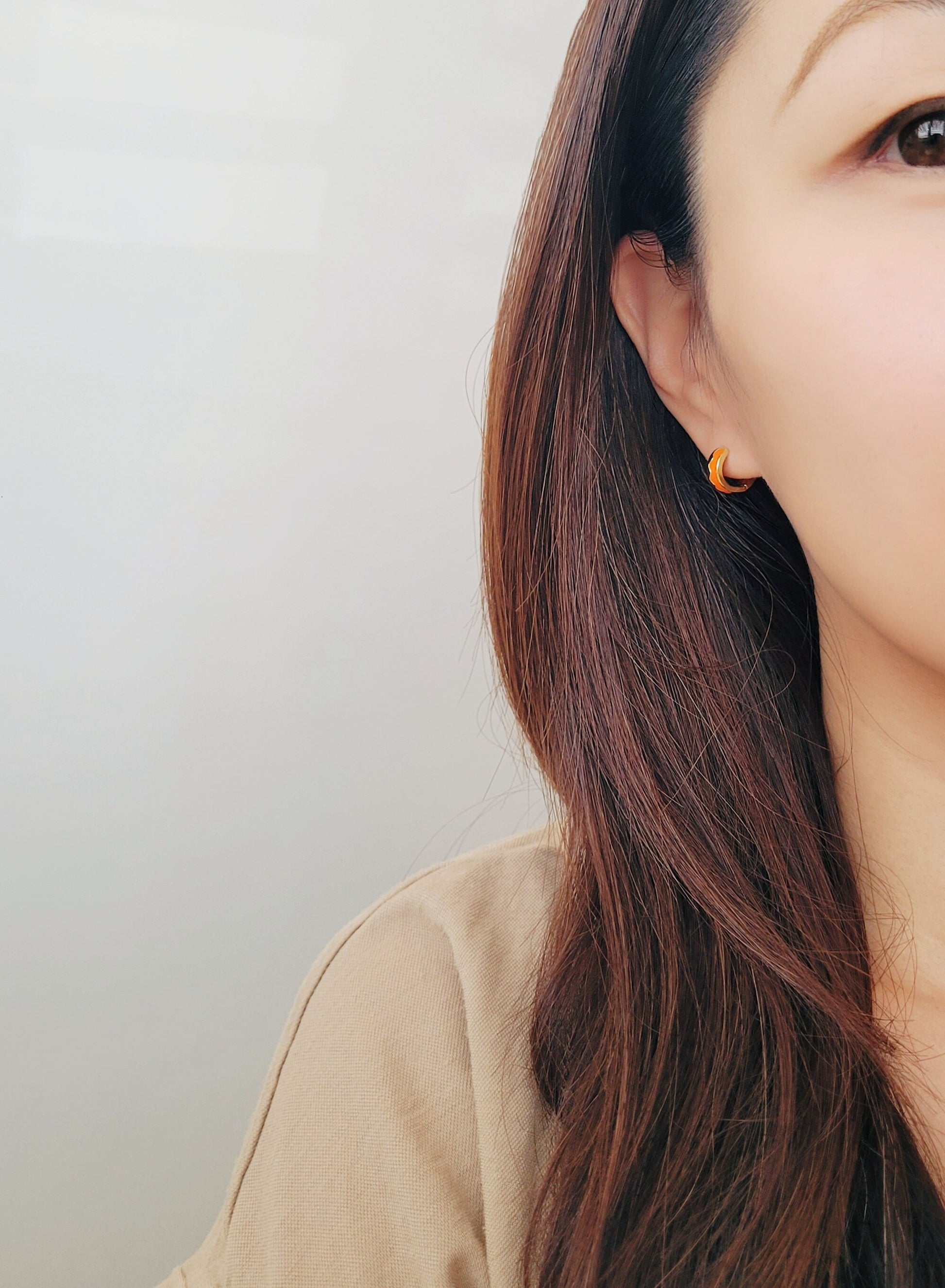 Close-up of a person wearing an orange earring with a plain background
