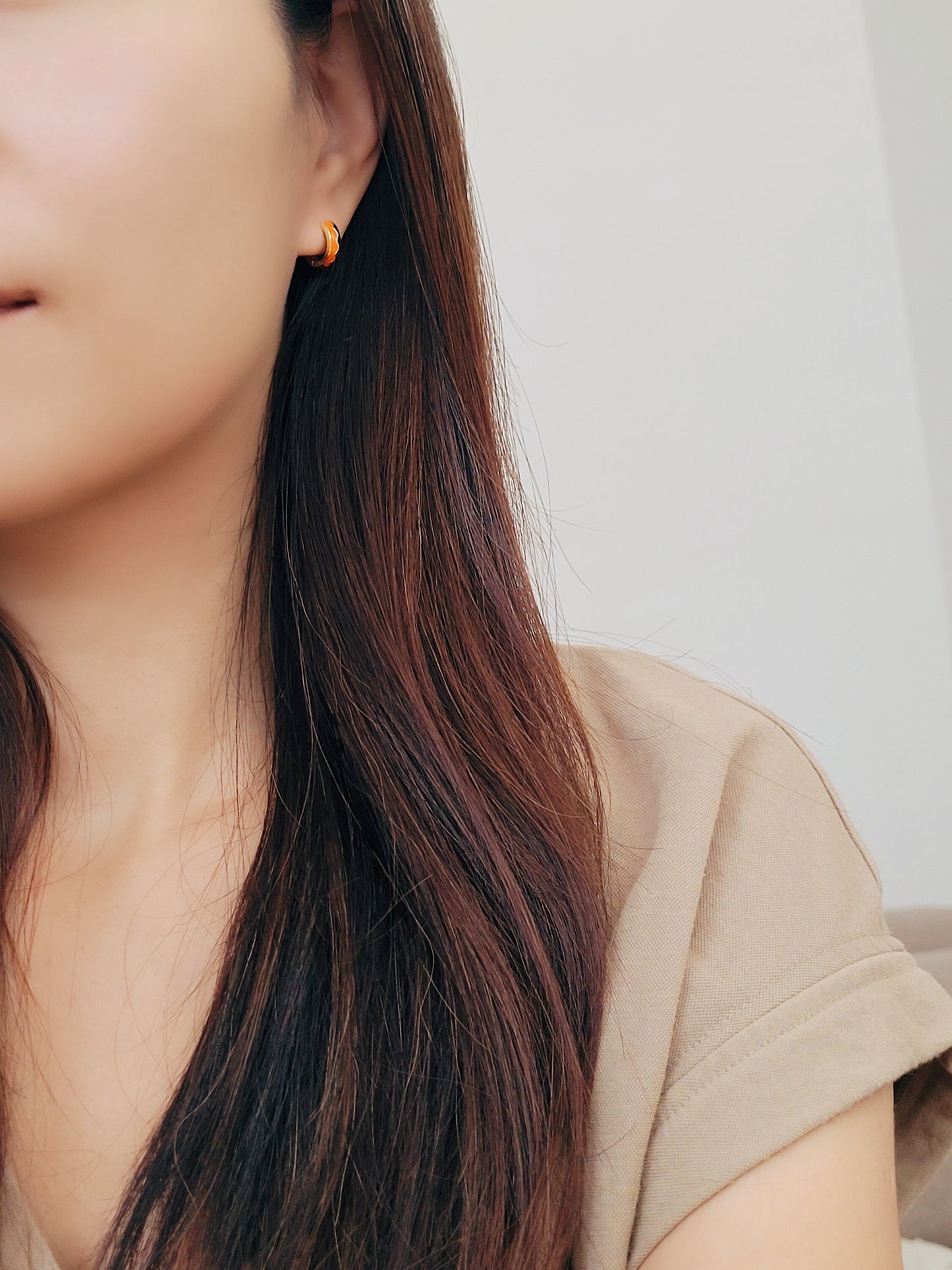 Close-up of a person wearing gold hoop earrings with a neutral background