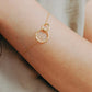 A delicate gold chain bracelet with two interlocking textured rings worn on a person's wrist, shown against a soft neutral background.