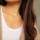 A lifestyle shot of a woman wearing a delicate gold chain necklace with a small white Opal pendant, styled over a white ribbed tank top and a beige cardigan.