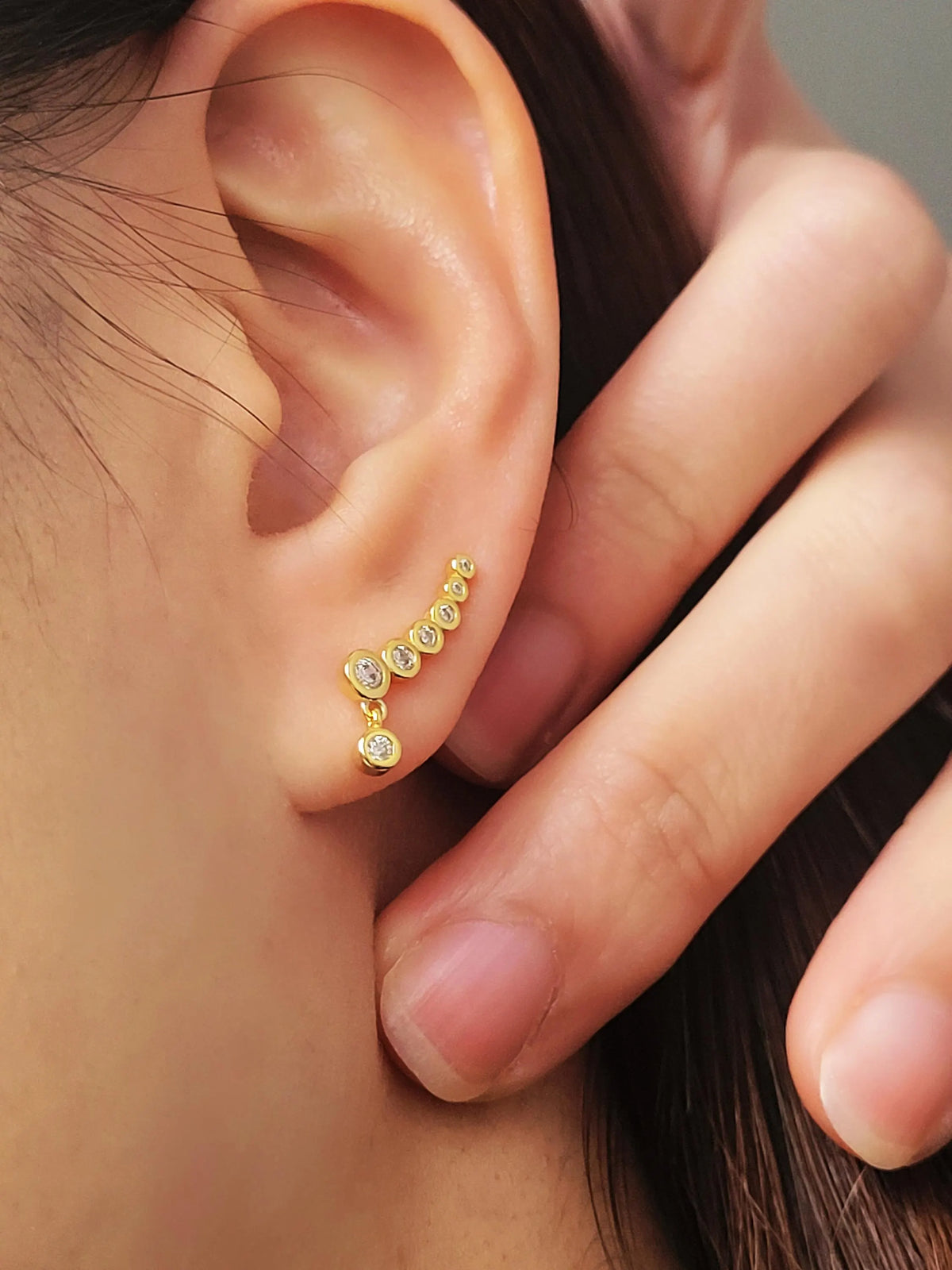 Woman wearing a gold cubic zirconia ear climber with graduated sparkling stones and a delicate drop detail.