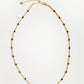 A delicate gold chain necklace with small, evenly spaced black beads, laid flat on a clean white background.