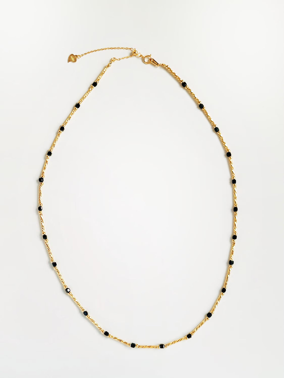 A delicate gold chain necklace with small, evenly spaced black beads, laid flat on a clean white background.