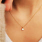 A close-up of a woman wearing a delicate gold chain necklace with a small white oval pendant.