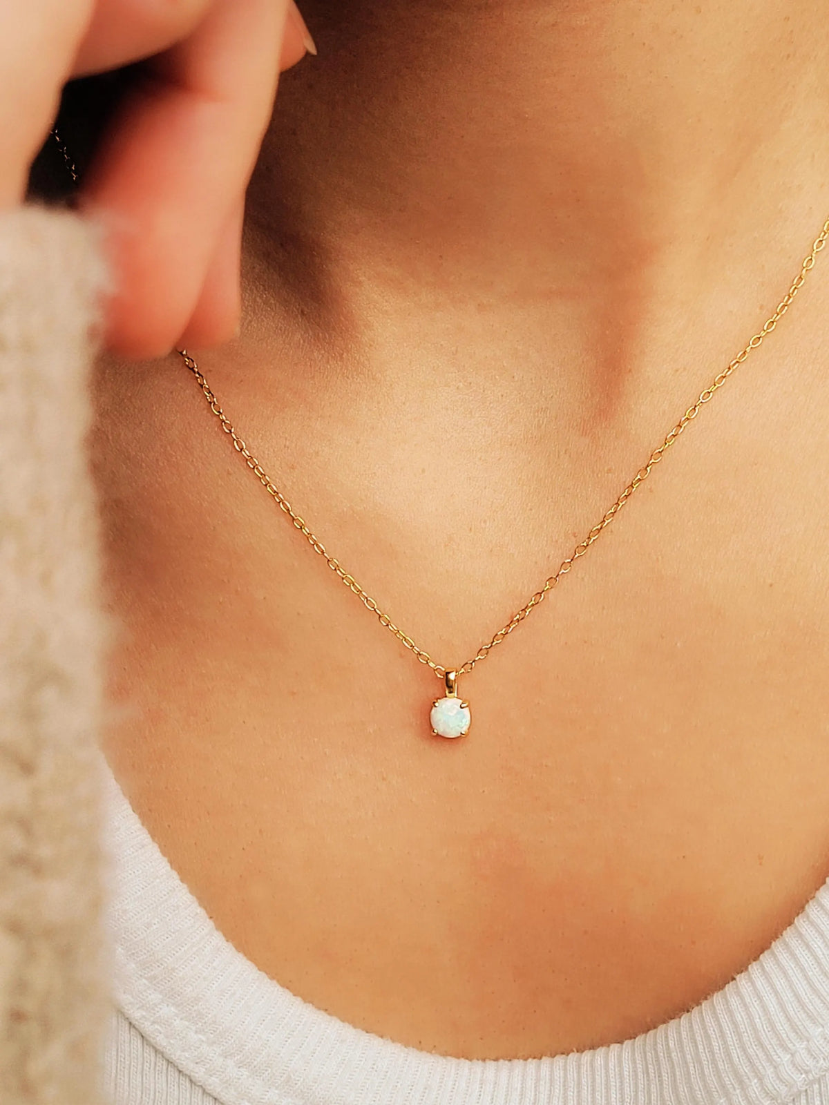 A close-up of a woman wearing a delicate gold chain necklace with a small white oval pendant.