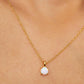 A delicate gold chain necklace with a small white opal pendant, worn on a girl's neck.