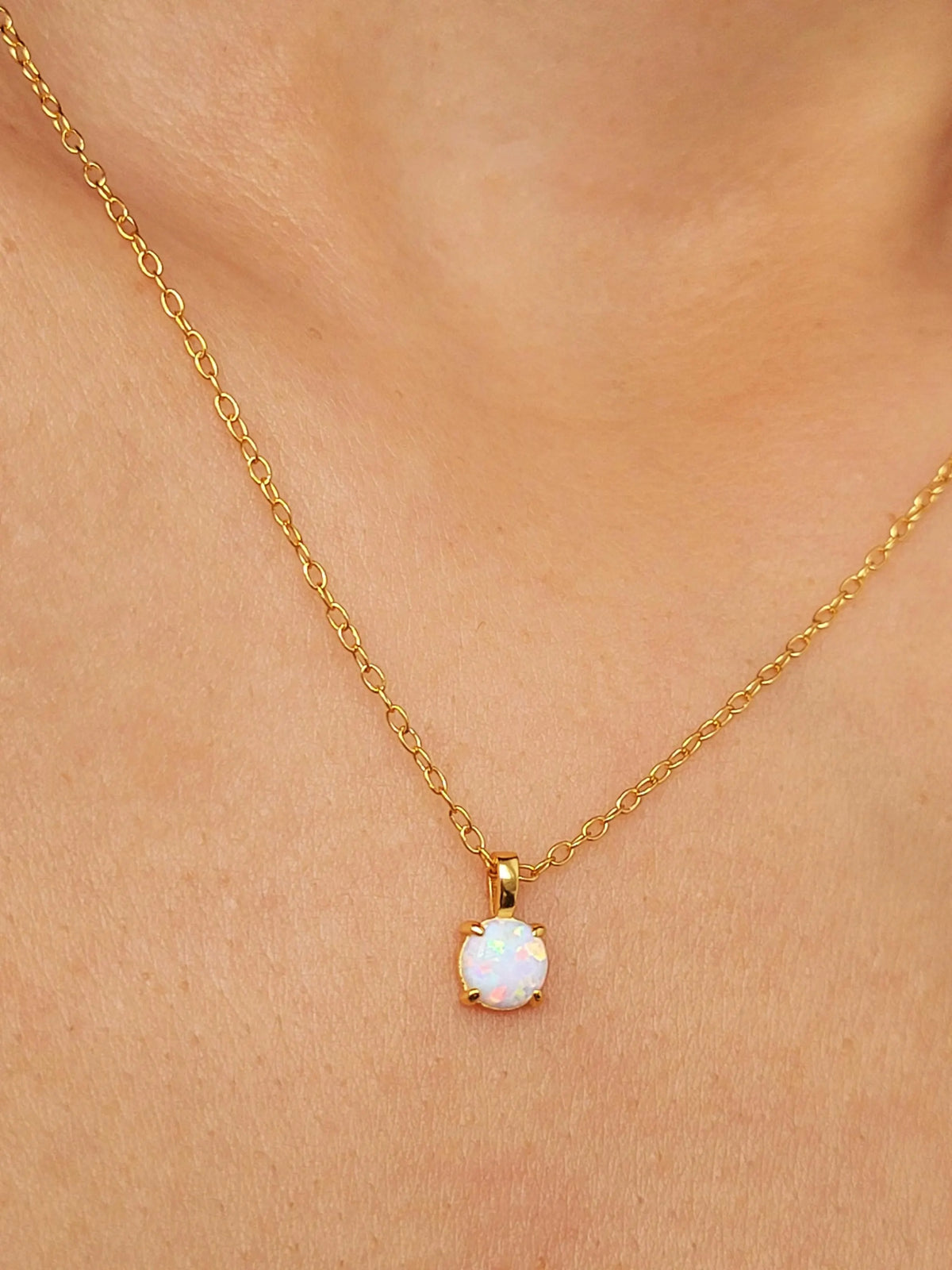 A delicate gold chain necklace with a small white opal pendant, worn on a girl's neck.