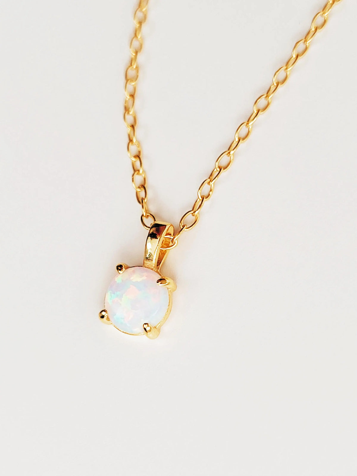 A gold chain necklace with a small oval pendant featuring a white opal gemstone in a gold bezel setting, shown against a plain light background.