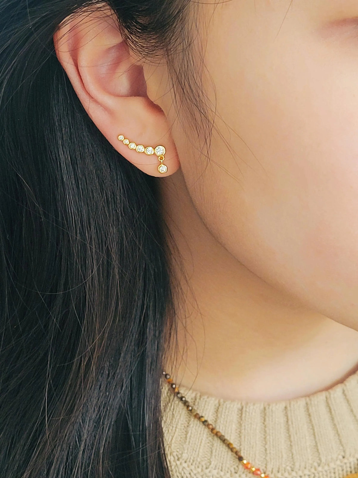 Close-up of a woman wearing a dainty gold bubble climber earring that follows the curve of her earlobe.