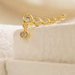 Close-up of a gold bubble climber earring displayed on a cream jewellery stand, showing its graduated stones and dangling charm.