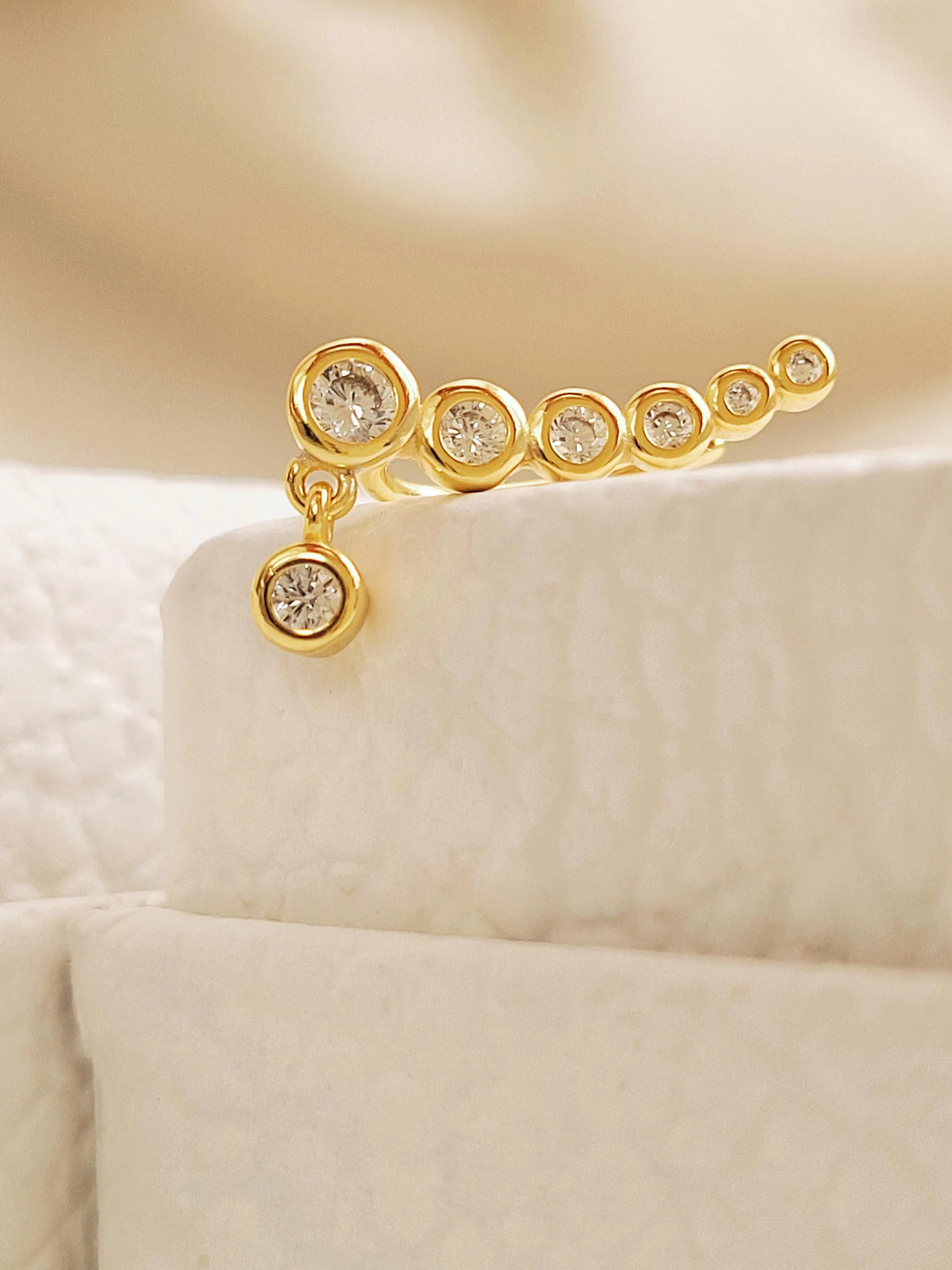 Close-up of a gold bubble climber earring displayed on a cream jewellery stand, showing its graduated stones and dangling charm.