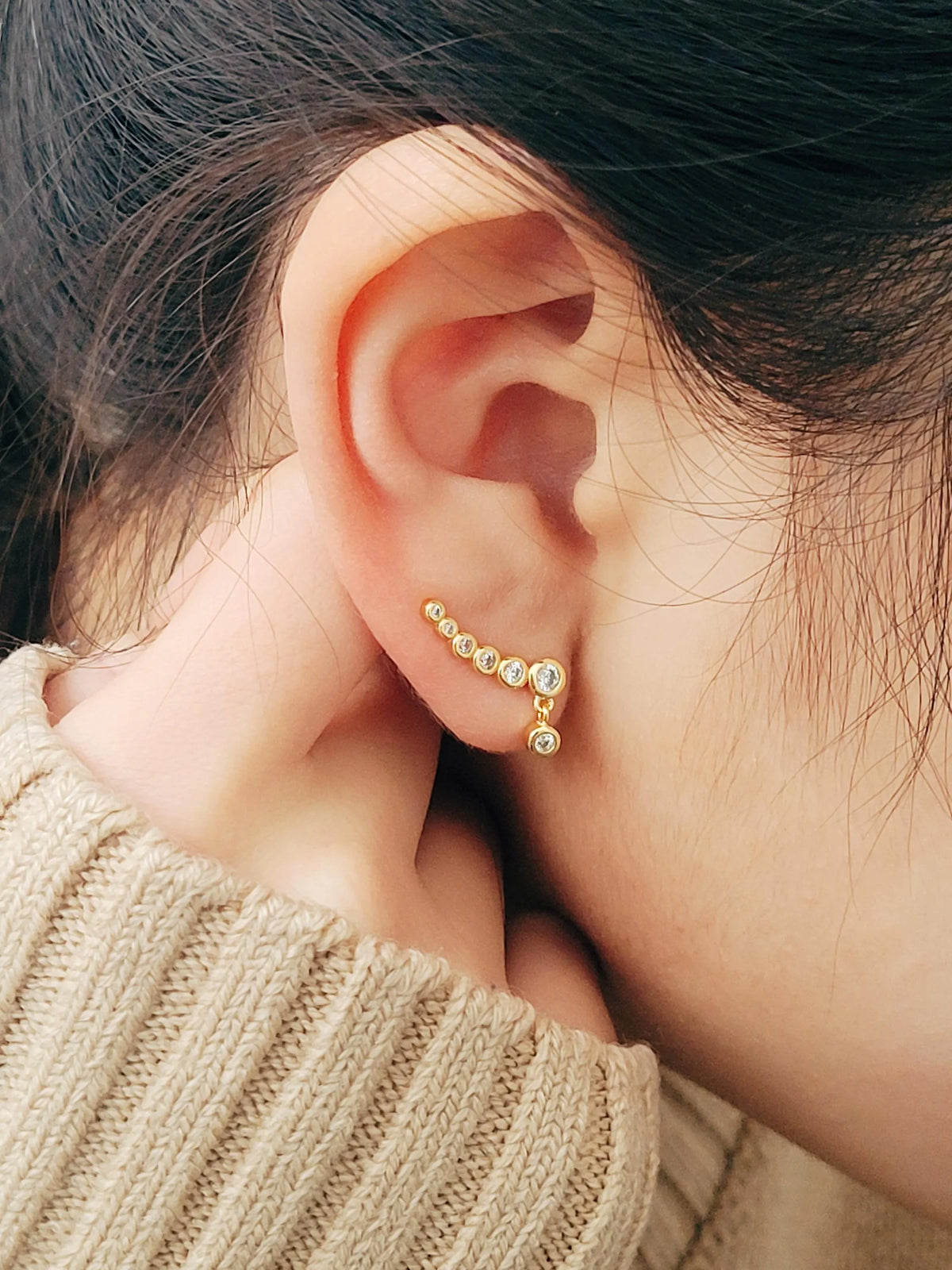 Close-up of a women's ear wearing gold crawler earrings with sparkling cubic zirconia stones, showcasing a minimalist and elegant ear climber design. Crafted in gold plated sterling silver.