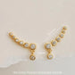 Pair of gold bubble ear climber earrings with sparkling round cubic zirconia stones displayed on a light neutral background.