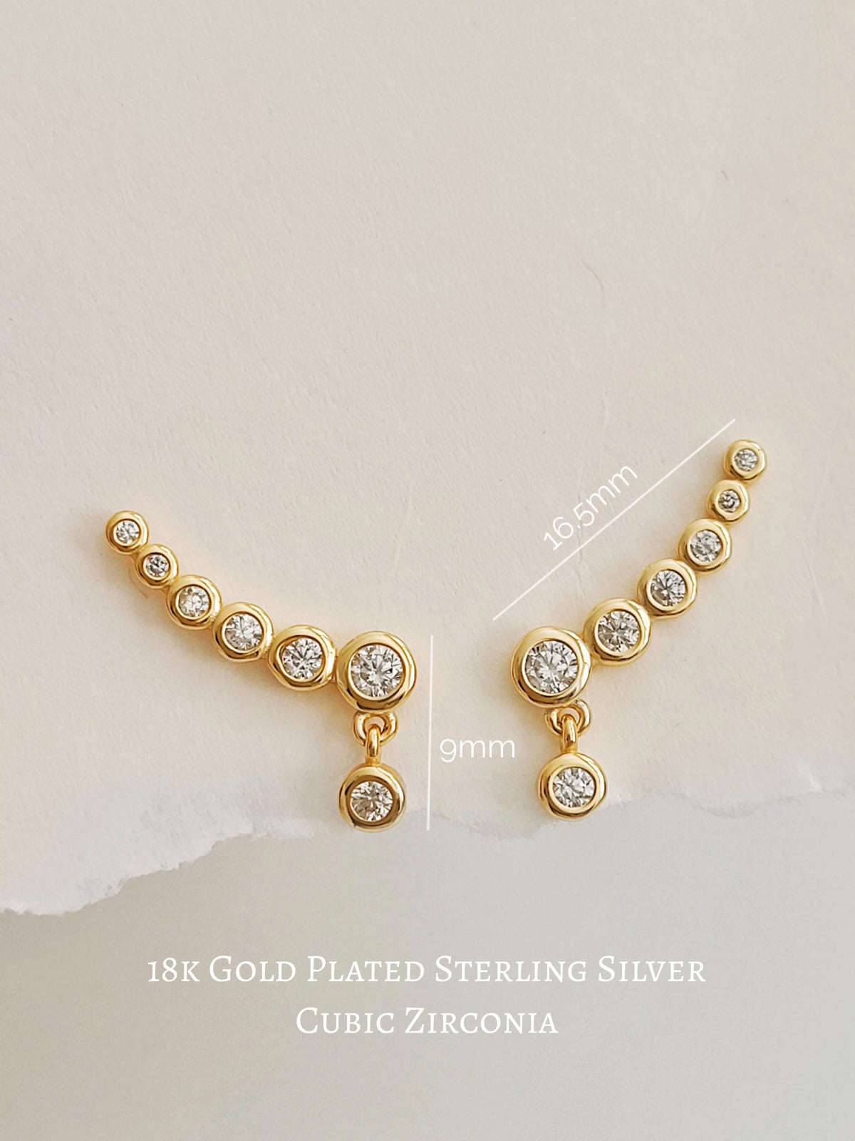 Pair of gold bubble ear climber earrings with sparkling round cubic zirconia stones displayed on a light neutral background.