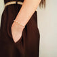 A close-up of a woman wearing a delicate pearl bracelet on her wrist, paired with a dark brown dress and a woven belt.