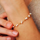 A delicate gold chain bracelet adorned with small tiny pearls, shown worn on a woman's wrist with fingers gently touching the band.