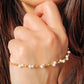 A close-up of a delicate gold chain bracelet adorned with small white pearls, worn on a woman's wrist.