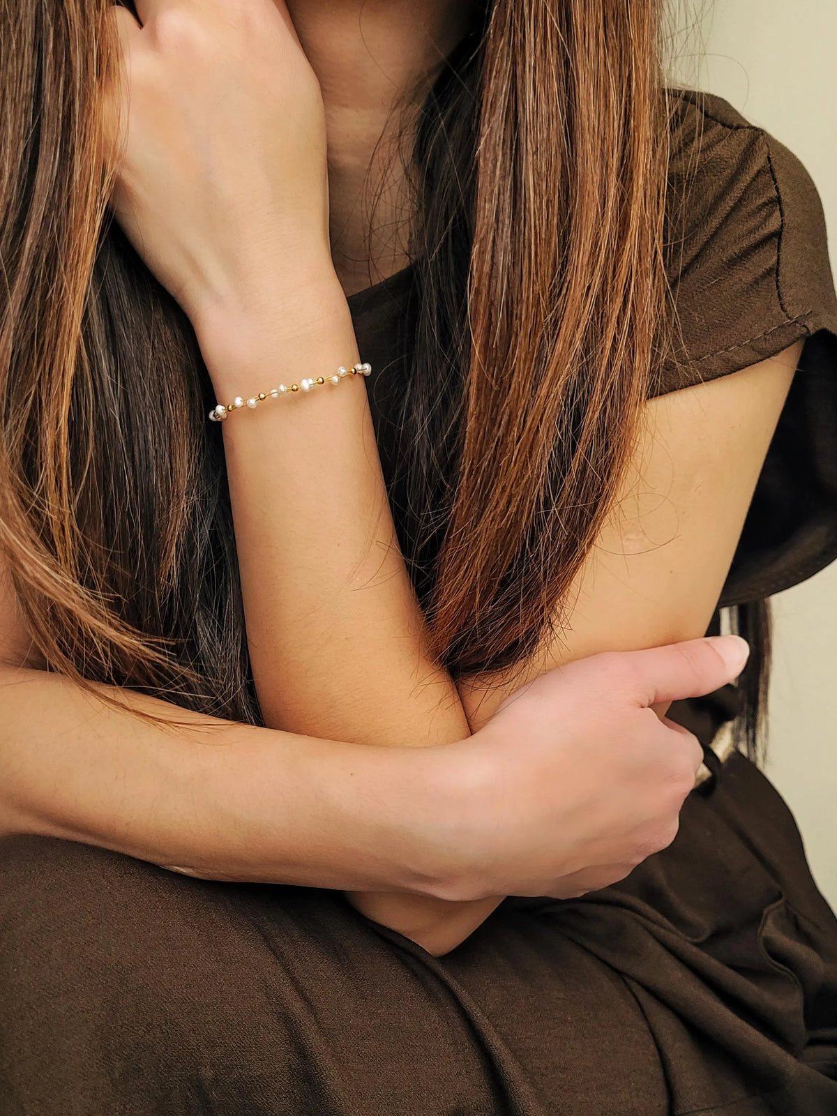 A delicate gold chain bracelet with small white natural pearl beads worn on a woman's wrist, shown in a close-up lifestyle shot.