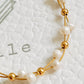 A close-up of a delicate gold wire bracelet with alternating white pearl beads and small gold spacer beads, laid on a textured white surface.