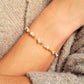 A delicate gold chain bracelet with small white pearl beads, shown worn on a person's wrist against a cozy gray knit sweater.