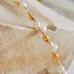 A close-up of a beaded bracelet with white freshwater pearls round beads and small polished gold spacer beads, draped over a light stone block.