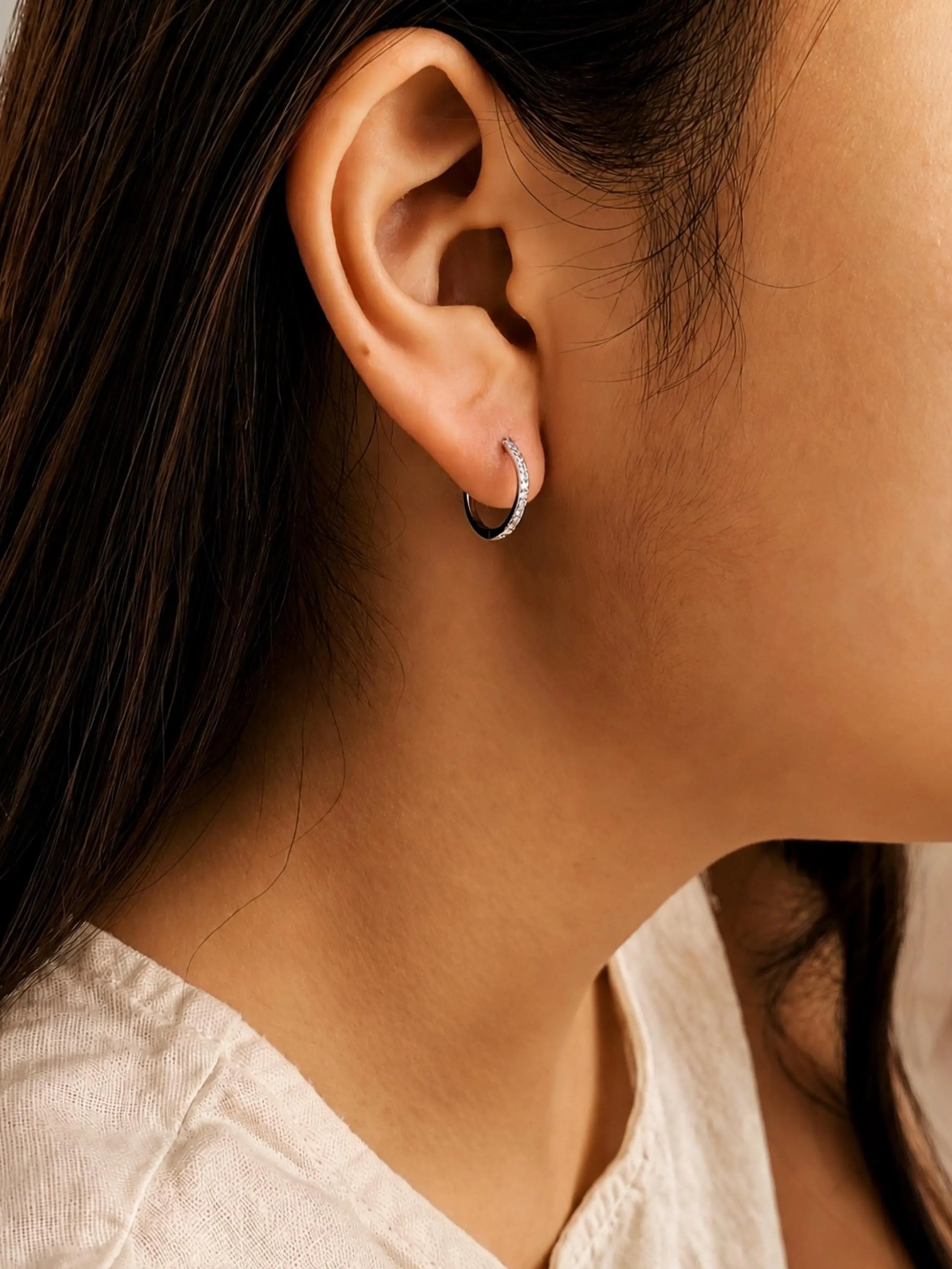 Woman wearing pavé-set hoop, often featuring clear cubic zirconia stones in a 925 silver setting. These are classic, versatile pieces known for their subtle sparkle, perfect everyday earrings.