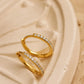 A pair of thin, hinged huggie hoop earrings in gold vermeil featuring a row of sparkling, clear cubic zirconia stones displayed on a luxury beige flower plate.