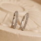 A pair of sterling silver huggie hoop earrings adorned with cubic zirconia, a versatile style designed to "hug" the earlobe. They feature a row of round-cut stones set into a silver band with a secure hinged closure. Perfect gift for her
