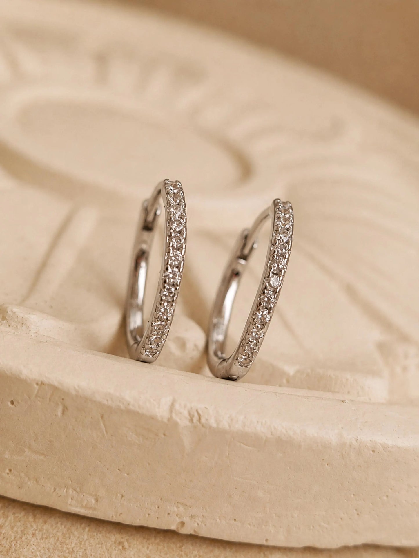 A pair of sterling silver huggie hoop earrings adorned with cubic zirconia, a versatile style designed to "hug" the earlobe. They feature a row of round-cut stones set into a silver band with a secure hinged closure. Perfect gift for her