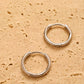 A pair of dainty gold huggie earrings featuring irregular organic shape with hinged snap closure on a beige color stone surface.